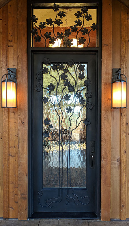 Close-up of door to the left, custom iron door with transom, stylized scrub oak with hand-cast iron leaves, branches and roots, clear glass, Patented Thermal Break, Hand Rubbed Bronze finish