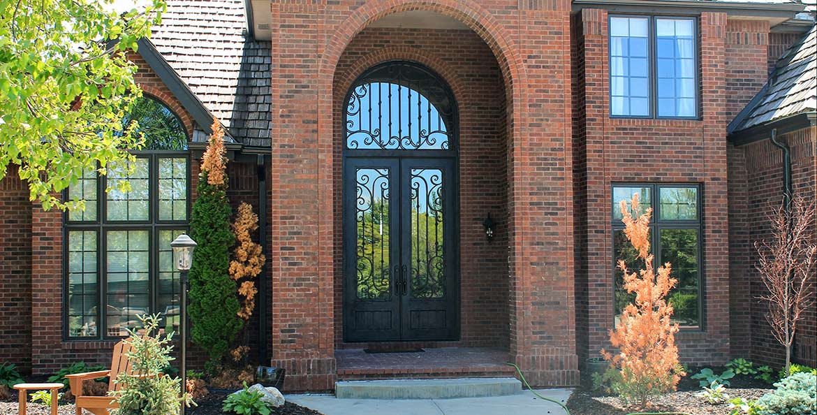 Site photo of brick home with large custom iron half-round transom and tall double doors, Milan series, Clear glass, Patented Thermal Break, Hand Rubbed Bronze finish